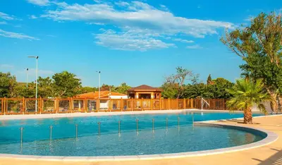 a large swimming pool with a house in the background at Cathy & David-Mobile Home 11-Camping Novela in Port-la-Nouvelle