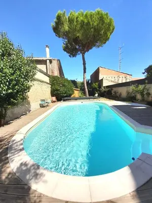 a large blue swimming pool with a tree in the background at La pause sous le pin B&B Chambres d'hôtes in Capestang
