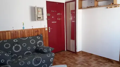 a living room with a couch and a red door at Studio Plage 200m Parking gratuit Port la Nouvelle in Port-la-Nouvelle