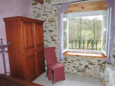 a room with a window and a chair and a cabinet at Gîte LA FENIAL in Montredon-Labessonnié