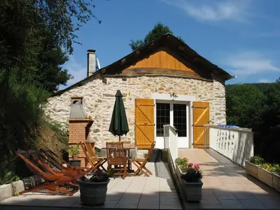 a stone cottage with chairs and an umbrella on a patio at Gîte LA FENIAL in Montredon-Labessonnié