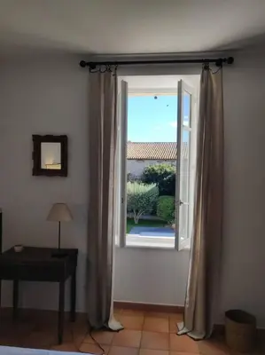 a window with curtains in a room with a table at La Maison de Colette - Coeur de village in Cuxac-dʼAude