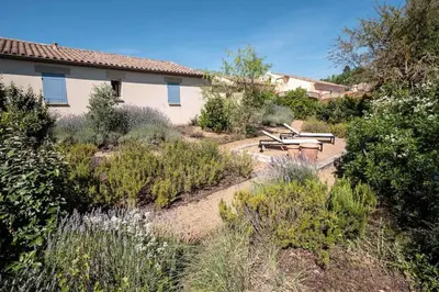 a garden with benches and plants in front of a house at Belle villa moderne 3 chambres, jardins terrasse piscine in Durban-Corbières