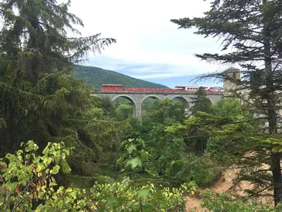 a red train crossing a bridge over a river at Chalet de charme in Montfort-sur-Boulzane