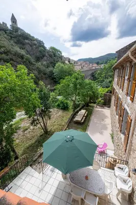 a patio with a green umbrella and tables and chairs at La Mazette, les pieds dans l'eau ! Privatisée ! 16 Pers in Olargues