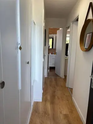 a hallway with white walls and wooden floors and a mirror at Le zéphyr in Gruissan
