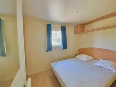 a bedroom with a bed and a window with blue curtains at Camping Caramany, Lac à proximité - Cabanes perchées - Mobil-homes - Emplacements nus pour camping-cars, tentes, caravanes in Caramany