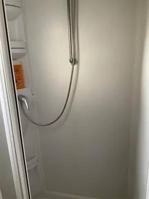 a shower stall with a hose attached to a wall at Mobilhome « Candice » in Sigean