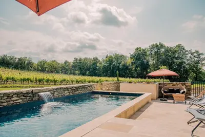 a swimming pool with a waterfall and an umbrella at Le mas de l'ecluse in Caux-et-Sauzens
