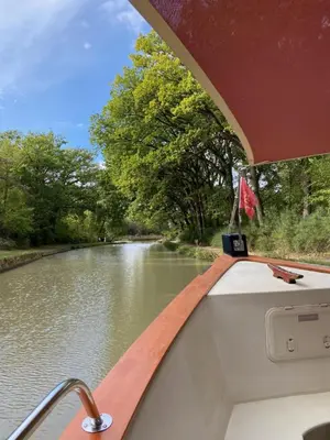 a boat on a river with a flag on the side at Gîte - Le Relais d'Affiac in Peyriac-Minervois