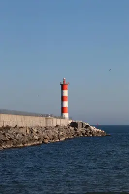a red and white lighthouse on a rocky island in the water at Agréable Studio en bord de mer in Port-la-Nouvelle