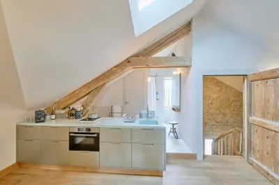 an attic kitchen with white cabinets and a wooden door at Dépendance de Sibra in Lagarde