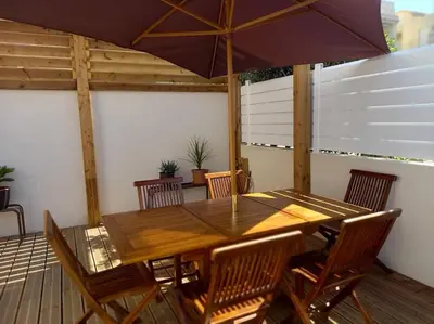 a wooden table with chairs and an umbrella on a deck at Appartement 100 m2 Terrasse Piscine in Gruissan