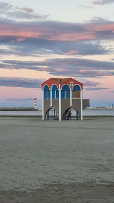 a building on the beach with a lighthouse in the background at Appart T2 vue imprenable sur le canal et la mer in Port-la-Nouvelle