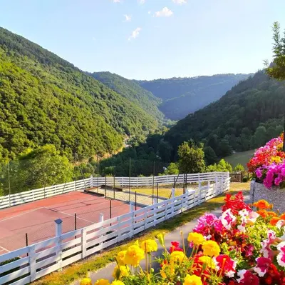 a tennis court with flowers and mountains in the background at La Vallée in Lacrouzette