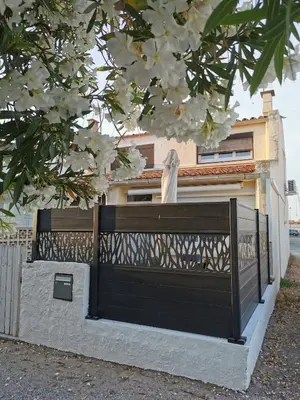 a black gate in front of a house with a flowering tree at Pavillon T3 proche de la plage TERRASSE GARAGE PARKING in Port-la-Nouvelle