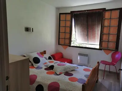 a bedroom with a bed and a chair and a window at villa plain pied 4 chambres à 100m de la plage in Port-la-Nouvelle