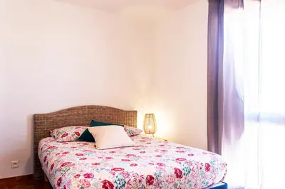 a bedroom with a bed with a floral bedspread and a window at Appartement moderne vue mer à Port-la-Nouvelle — 42 m² in Port-la-Nouvelle