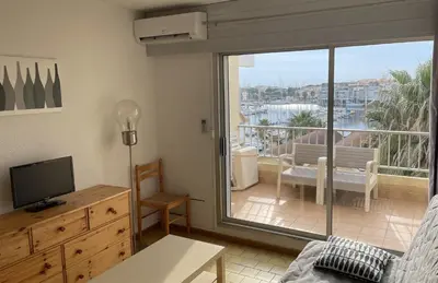 a living room with a television and a balcony at Vue ensoleillée sur le port de Gruissan in Gruissan