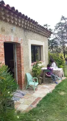 a woman sitting at a table in front of a house at la Bergerie in Salles-sur-lʼHers