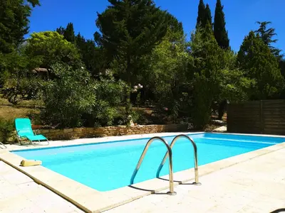a blue swimming pool with a chair and trees at Chambre Indépendante Piscine, Parc, Cuisine... in Brézilhac