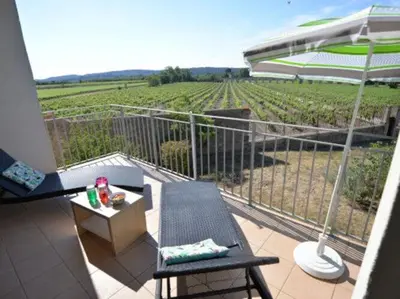 a balcony with a table and an umbrella and a vineyard at Apartment in Azille near Lac de Jouarres in Azille