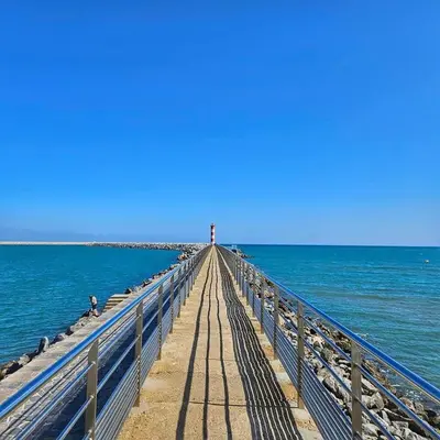 a pier stretches out into the ocean with a lighthouse at Les mobil homes de NOLY TV CLIM 6places in Port-la-Nouvelle