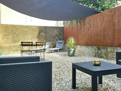 a patio with chairs and tables and a black umbrella at Superbe Appt avec cour et parking gratuit à 5min de la cité médiévale in Carcassonne