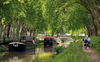 a river with a bridge and people riding bikes on a canal at Evasion dépaysante Canal du Midi * Terrasse & SPA in Castelnaudary